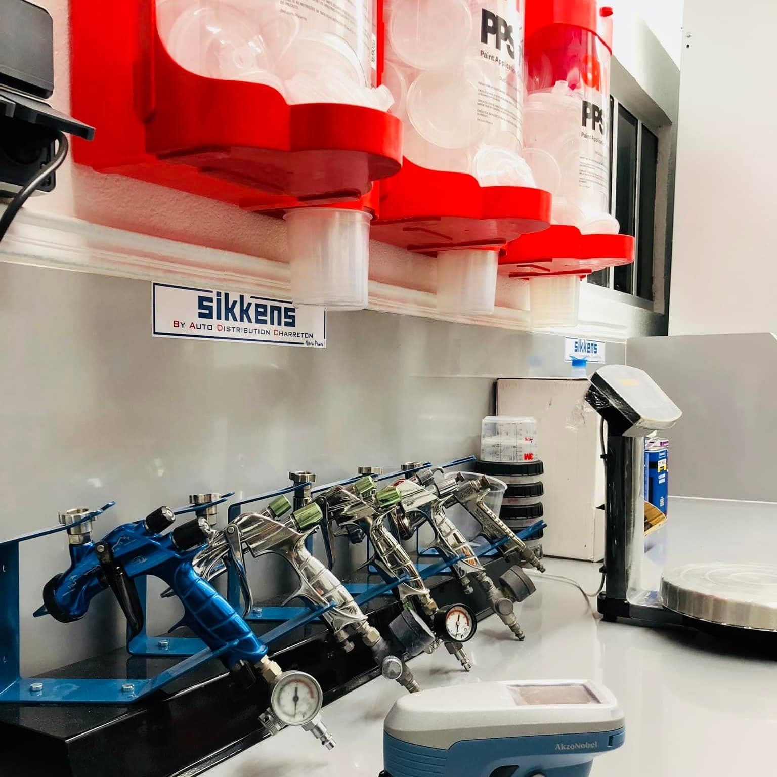 Le laboratoire de peinture : pistolets à peinture alignés, godets PPS, balance de pesée et distributeur de teintes Sikkens.