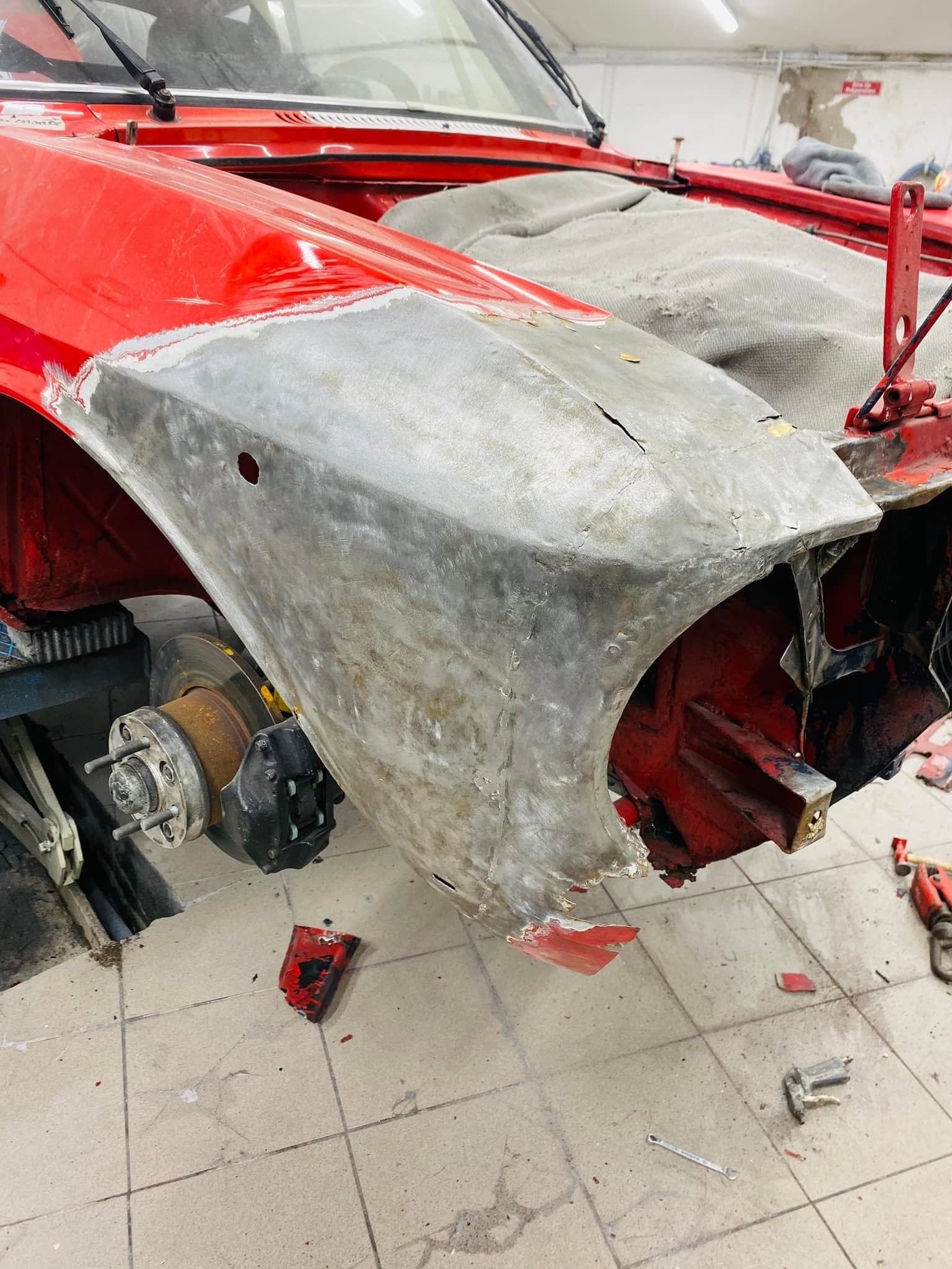 L’aile de l’Alfa Romeo mise à nu après planage : la tôle brute apparaît sur toute la surface réparée.
