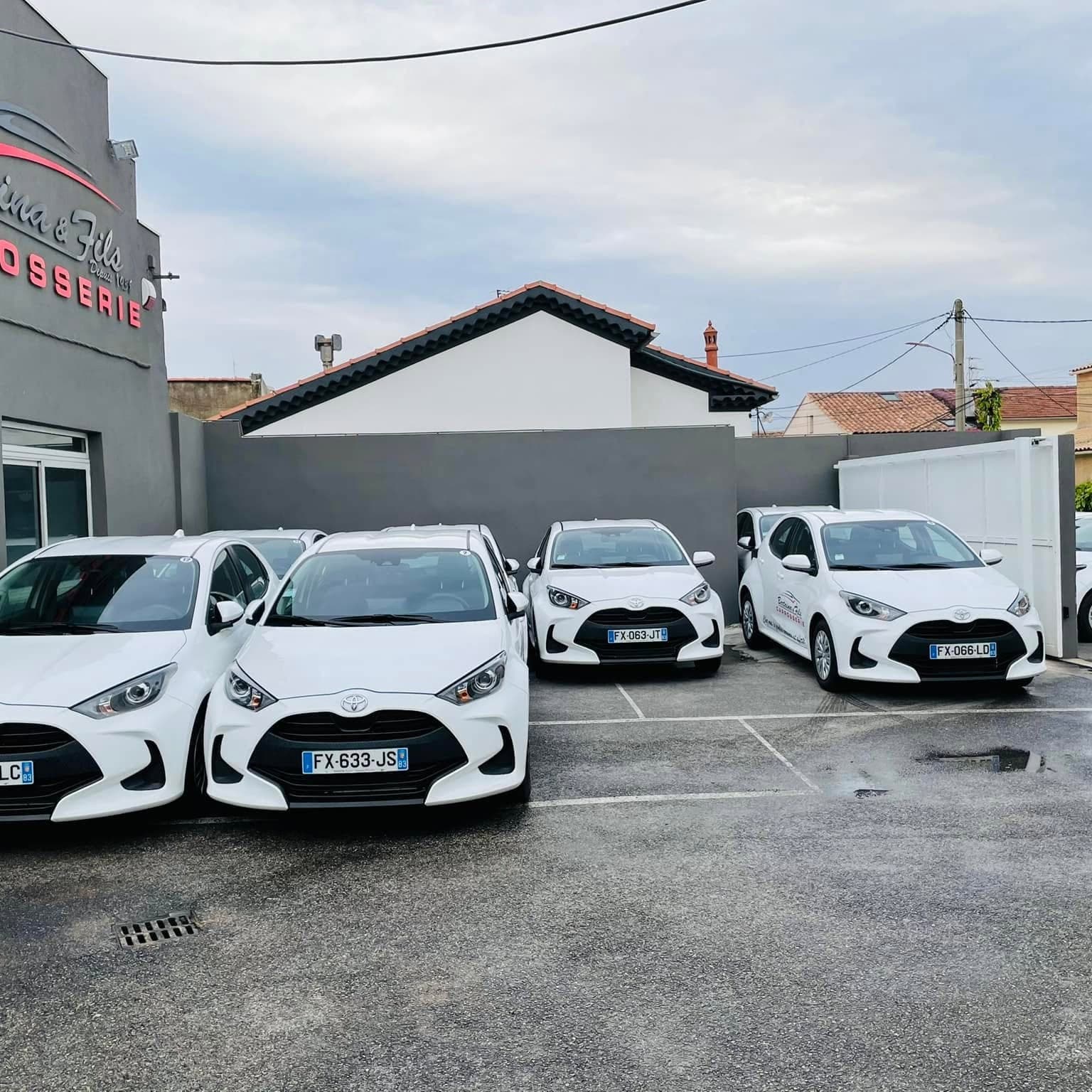 Cinq Toyota Yaris blanches de courtoisie alignées sur le parking de la carrosserie Bertaina et Fils.